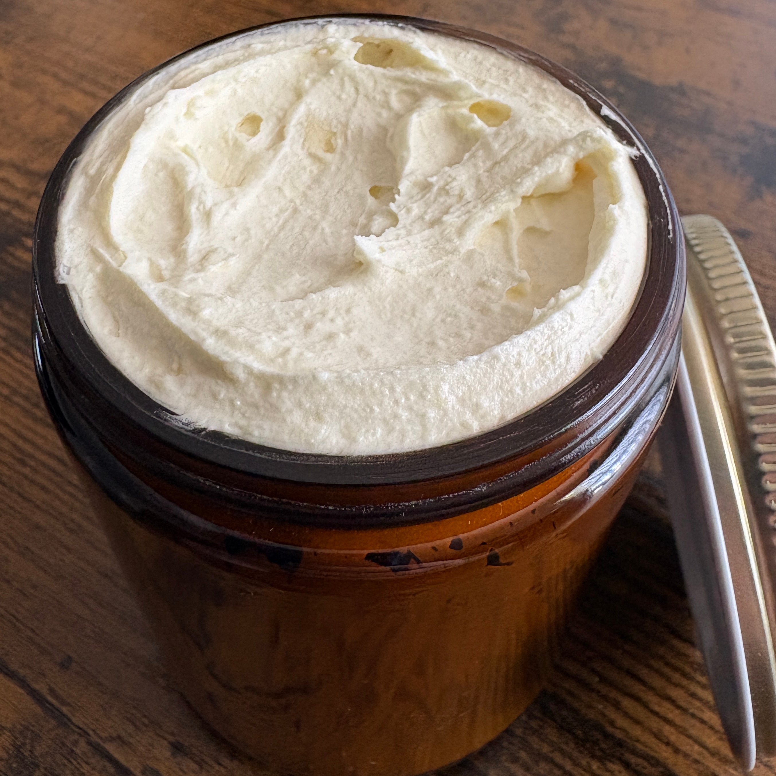Jar of white cream with a metal comb on a wooden surface